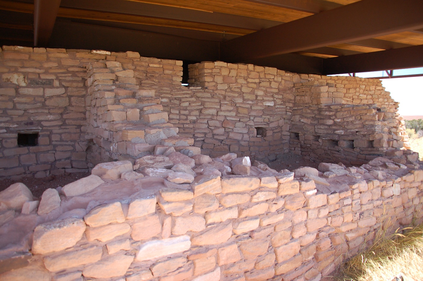 A stone wall in front of a brick building

Description automatically generated